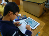 写真:タブレットPCを見ながらノートで計算する子ども