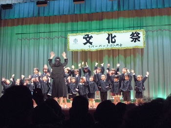 写真:ステージで両手をあげて歌う子どもたち