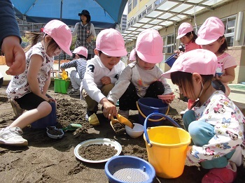 写真:帽子をかぶって砂遊びをする子どもたち