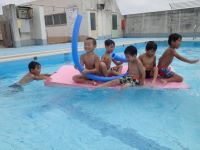写真:板に乗ってプールに浮く子どもたち