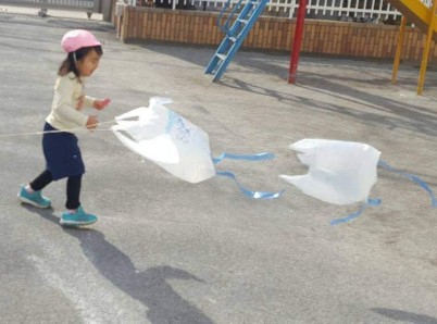 写真:風になびくビニール袋の凧を見る子ども