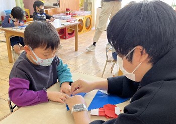 写真:先生と一緒に折り紙を折る子ども