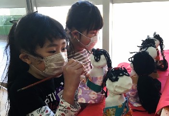 写真:人形の髪の毛を束ねる子どもたち