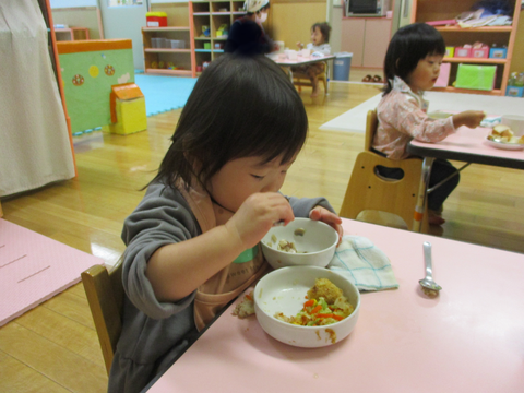 器に手を添えてスプーンですくっている子ども