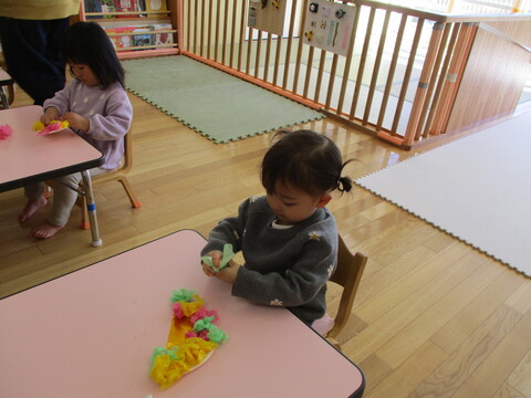 クシュクシュと丸めたお花紙(ピンク、黄色、黄緑)を紙皿に貼っていく子ども