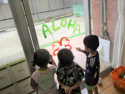 窓ガラスに絵の具で『ALOHA』とお絵描きされているのを不思議そうに見ている子ども