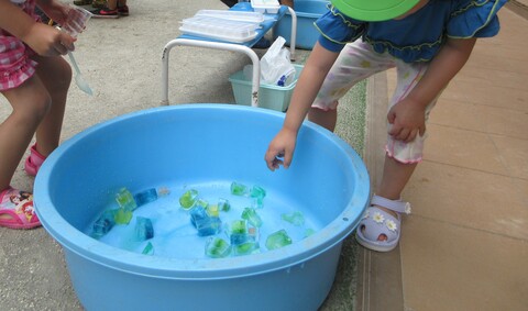 バケツに入っている色水で遊ぶ子どもたち